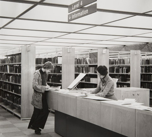 Black and white photo of a student and Librarian at a service desk, 1970's.