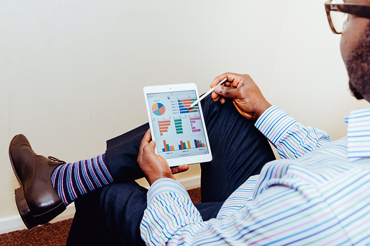 man looking at charts on a hand-held device. Photo by Adeolu Eletu on Unsplash.