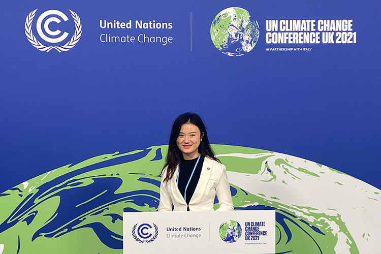 Elena Chen shown at COP26, in front of a banner of the Earth in space and the conference logos