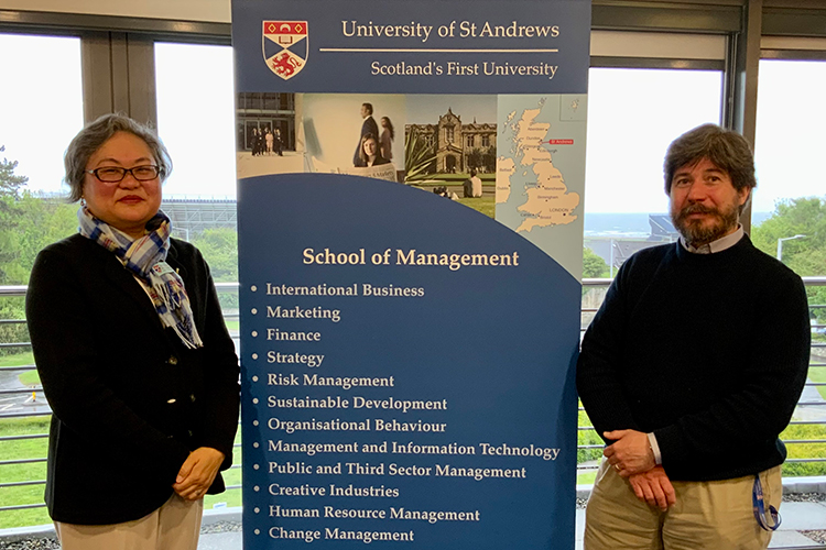 Helen Hwang and Tobias Jung stand either side of a University of St Andrews School of Management banner. Helen wears a scarf in the School's tartan.