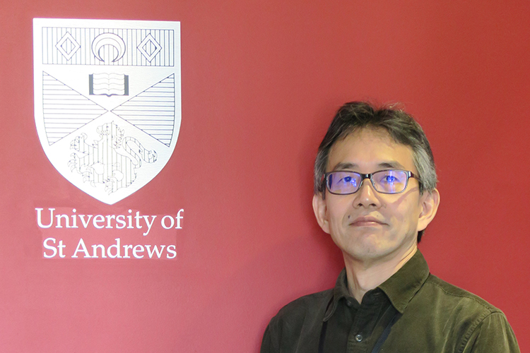 Arito Ono stands next to a wall which shows the crest of the University of St Andrews.