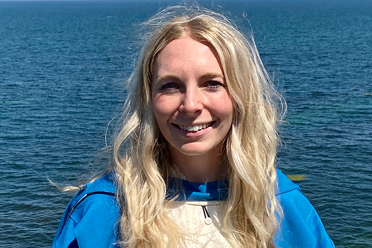 Meredith Schertzinger, smiling, shown in graduation gown with the sea in the background