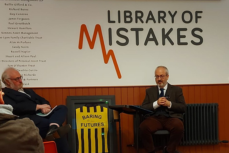 Philip Roscoe sits under a sign saying 'Library of Mistakes' and two people are shown listening to him speak