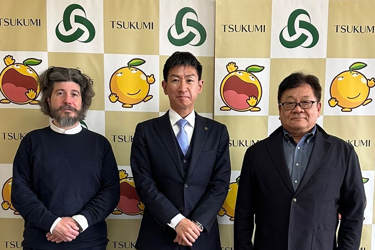 Professor Tobias Jung with two dignitaries in Japan. A banner in the backgroupn repeats the place name 'Tsukumi'.