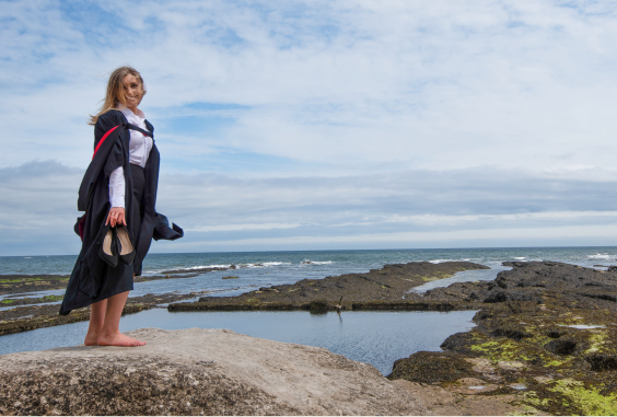 female student in robes standing on rocks