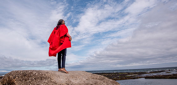 student in red gown on rock