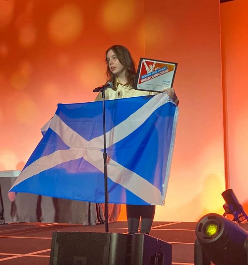 Lucy on stage with flag and competition certificate